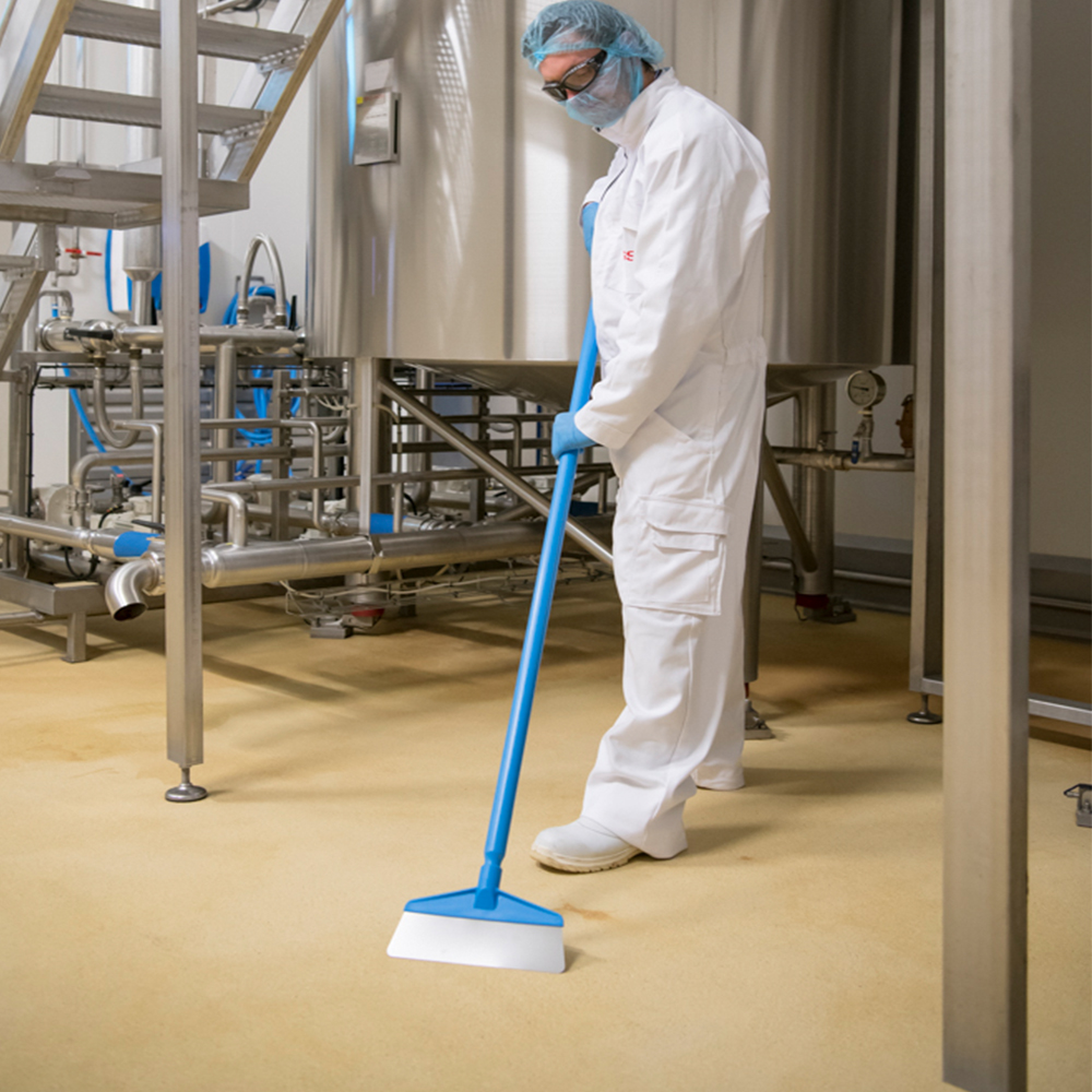 Hygienic Vikan floor squeegee in action in an industrial setting, used by a worker in protective clothing for optimal hygiene.