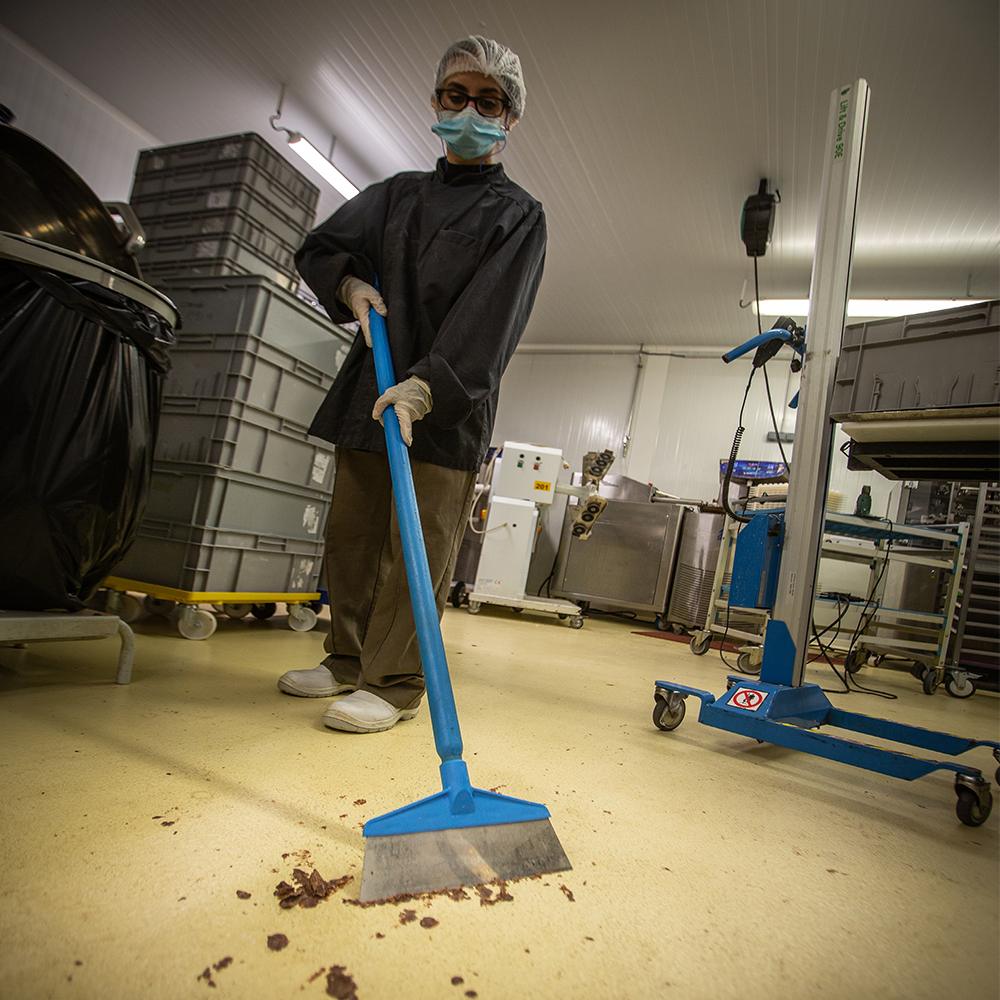 Worker in a food processing facility efficiently cleaning with a blue Vikan floor squeegee, removing debris and ensuring a clean workspace.