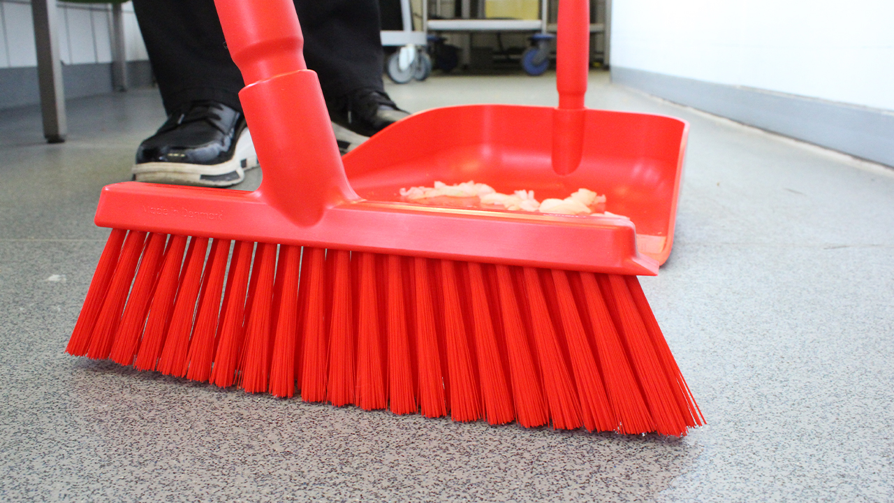 Red Vikan broom and dustpan close-up in use, ideal for hygienic zone separation.