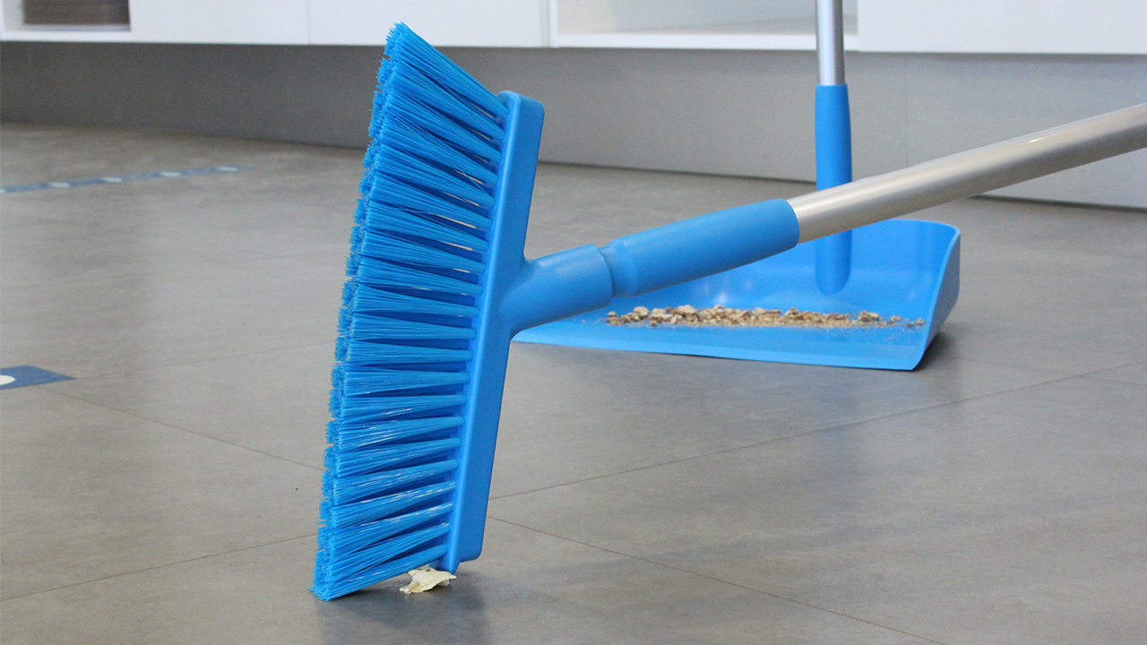 Blue Vikan broom sweeping debris into a dustpan in a clean and professional environment.