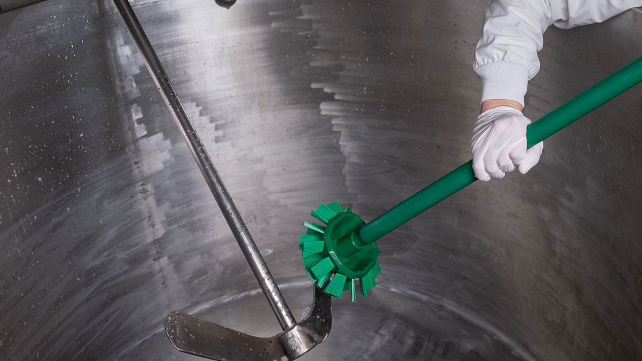 Food industry worker using a hygienic Vikan brush with a long handle for effective and safe cleaning in a stainless steel production environment