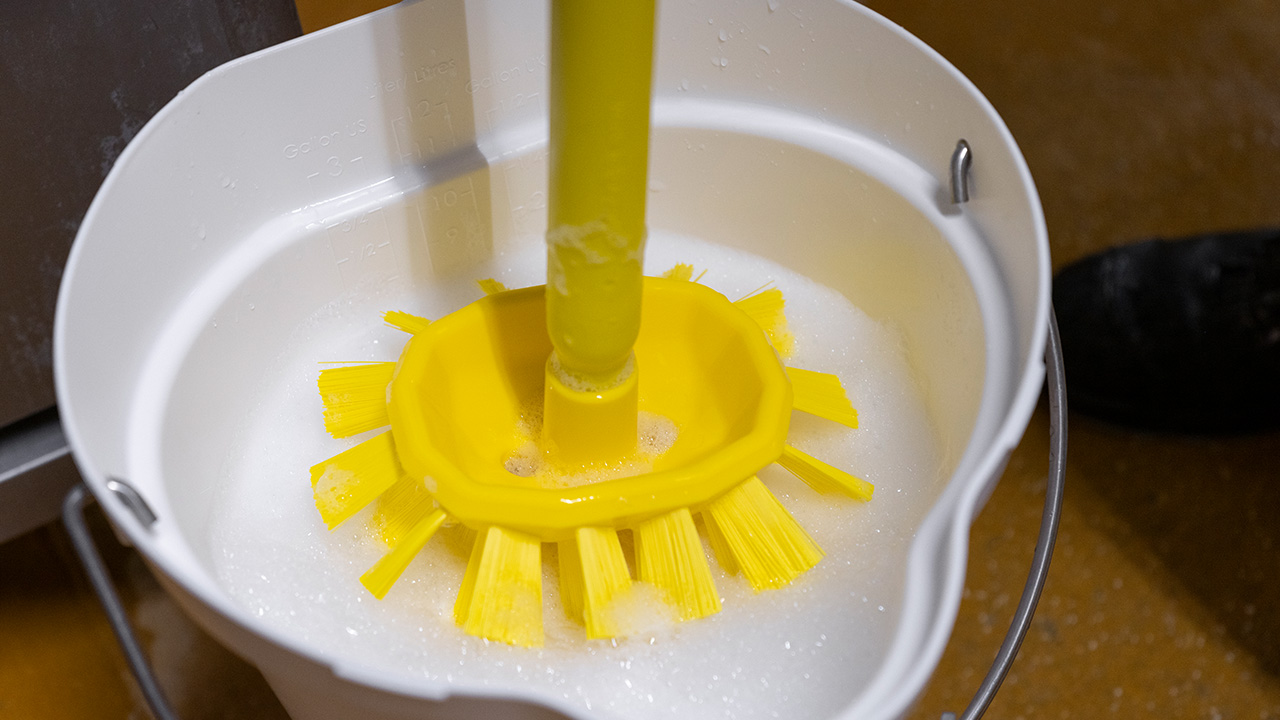 Hygienic yellow Vikan brush submerged in a soapy cleaning solution inside a white bucket, ensuring effective and safe cleaning