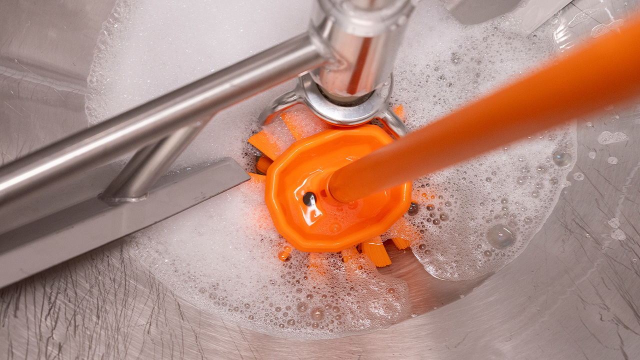Hygienic orange Vikan brush in action, effectively cleaning stainless steel equipment with soapy water for optimal hygiene.